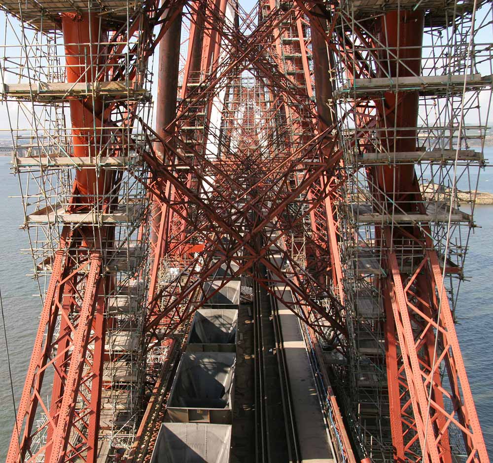 The Forth Rail Bridge  -  A train of empty coal wagons passes across the bridge beneath the scaffolding erected for painting