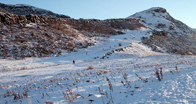 View from Hunter's Bog in Holyrood Park.  Walkers, one with a sledge, head towards the summit of Arthur's Seat