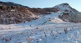 View from Hunter's Bog in Holyrood Park.  Walkers, one with a sledge, head towards the summit of Arthur's Seat