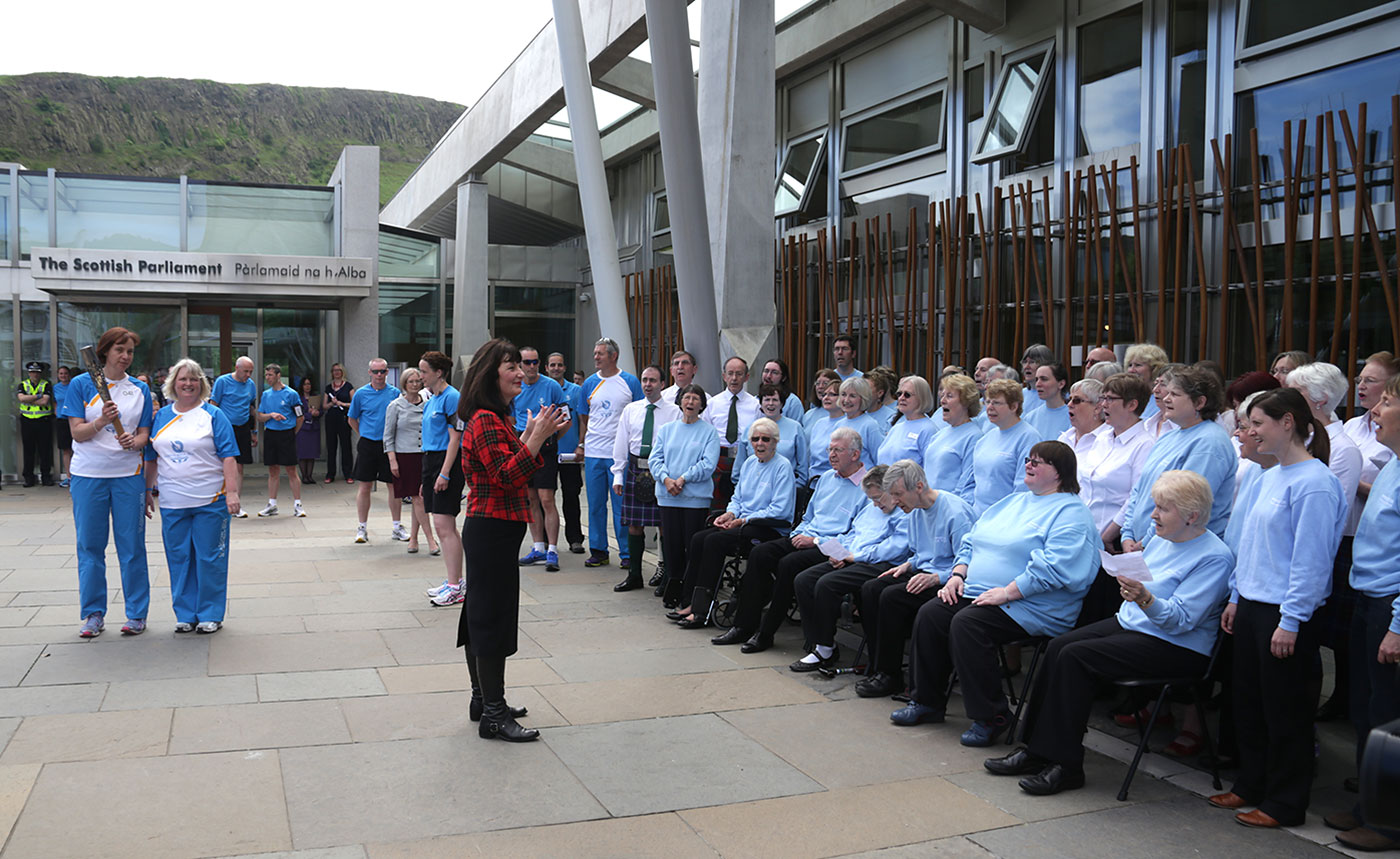 The Queen's Baton emerges from The Scottish Parliament in front of a choir singing in Gaelic