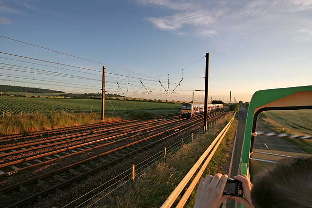 Open-top bus excursion to North Berwick - Approaching Drem heading west, as a train on the East Coast Main Line passes, heading to the east.