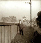 A railway worker stands beside the track as a train passes heading towards a signal box.  Where is it?
