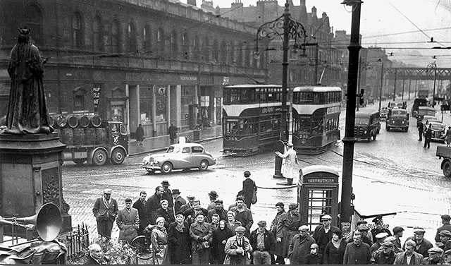 A crowd gathers at the foot of Leith Walk in May 1955. Who is in the crowd? Who was the speaker? There is an interesting mix of traffic in the background.