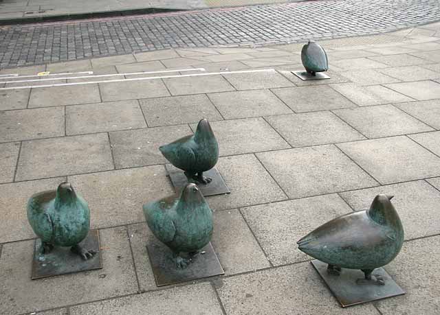 A flock of pigeons in bronze on the pavement at Elm Row