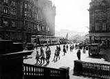 Black & white image derived from a colour photo taken from the steps of Register House, looking towards Edinburgh Castle with pedestrians at the East End of Princes Street in the foreground