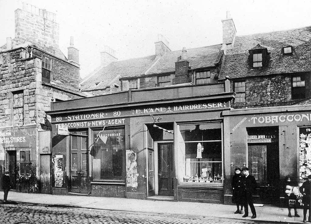 Where and when was this photograph of a row of shops, including E Kane, Hairdresser, taken?